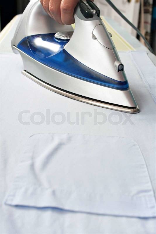 Closeup of and iron pressing and ironing a pocketed dress shirt on an ironing board, stock photo