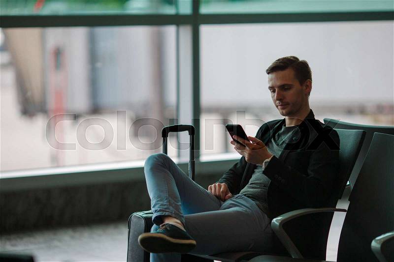 Urban business man talking on smart phone traveling inside in airport. Casual young businessman wearing suit jacket. Handsome male model. Young man with cellphone at the airport while waiting for boarding, stock photo