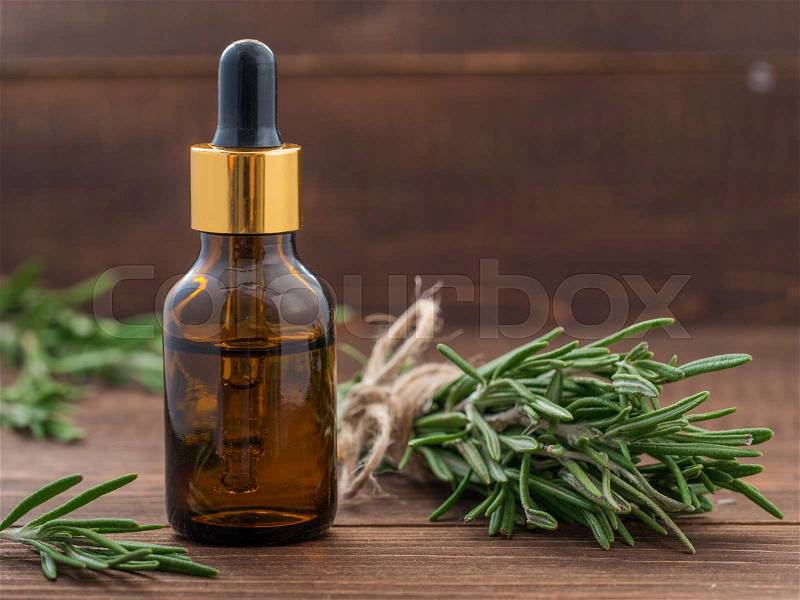 Rosemary essential oil in dark glass bottle and fresh rosemary on dark wooden background with copy space, stock photo