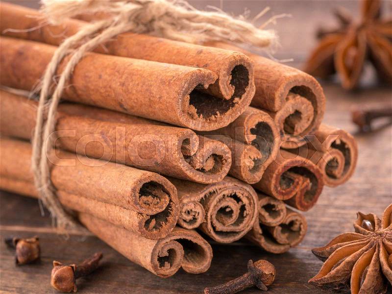 Ground cinnamon, cinnamon sticks, tied with jute rope on wooden background. Clove and star anise as background, stock photo