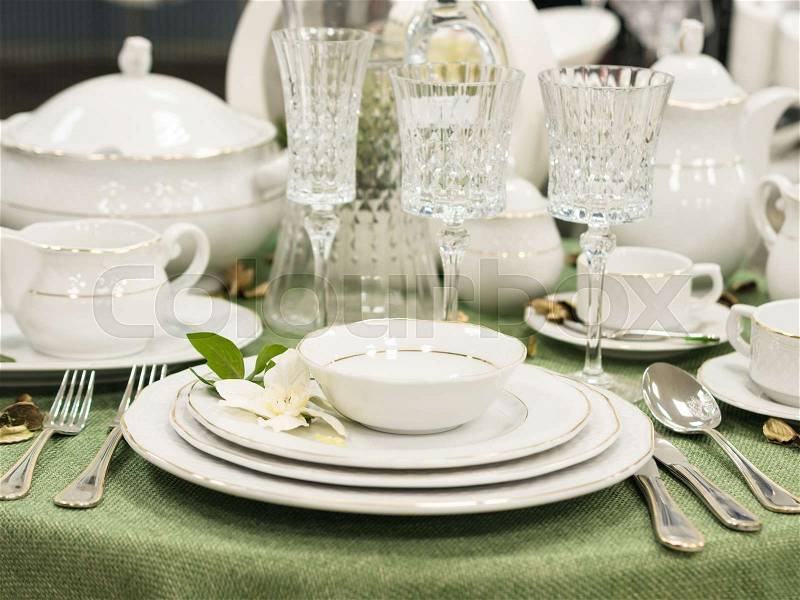 Set of new dishes on table with green tablecloth. Stack of white plates with flowers on restaurant table. Shallow DOF, stock photo