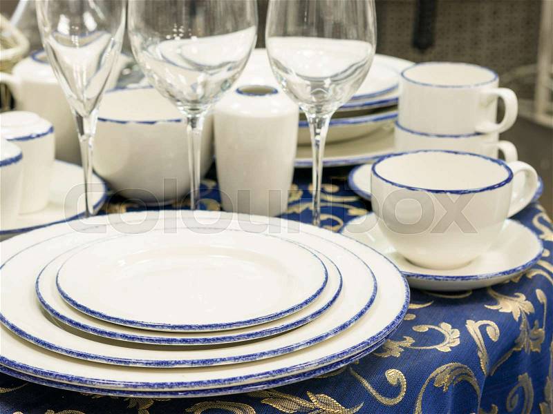Set of dishes close up on table with blue tablecloth. Stack of plates, wine glasses and cups on restaurant table. Shallow DOF, stock photo