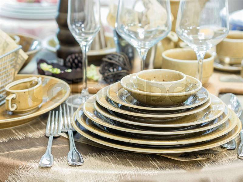 Set of new dishes on table with tablecloth. Stack of beige plates and wine glasses on restaurant table. Shallow DOF, stock photo