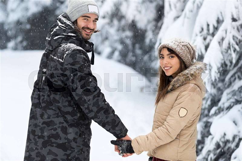 Young Romantic Couple Walking In Snow Forest Outdoor Mix Race man And Woman Holding Hands Winter Pine Woods, stock photo