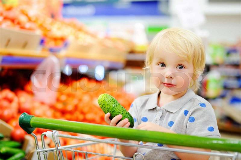 Cute toddler boy sitting in the shopping cart in a food store or a supermarket. Healthy lifestyle for young family with kids, stock photo