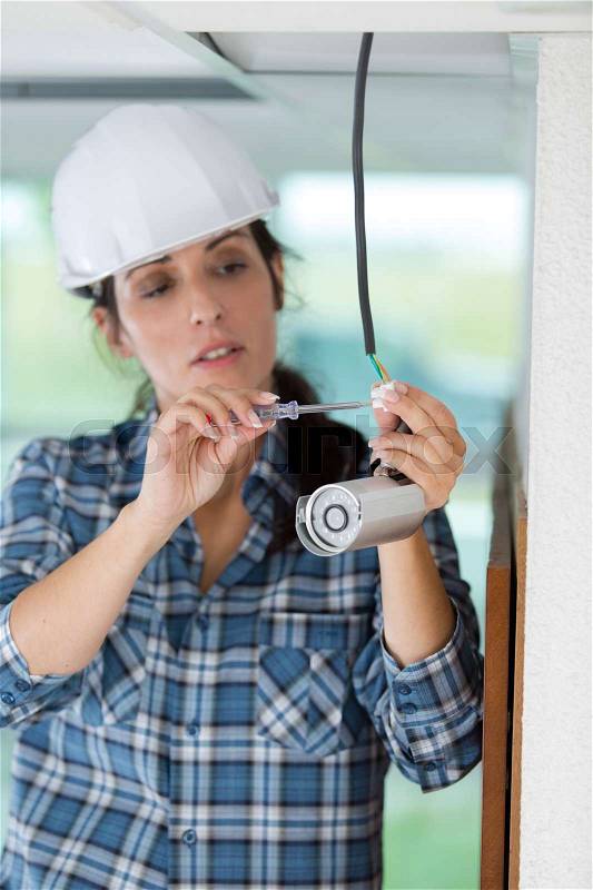 Female technician installing camera on wall with screwdriver, stock photo