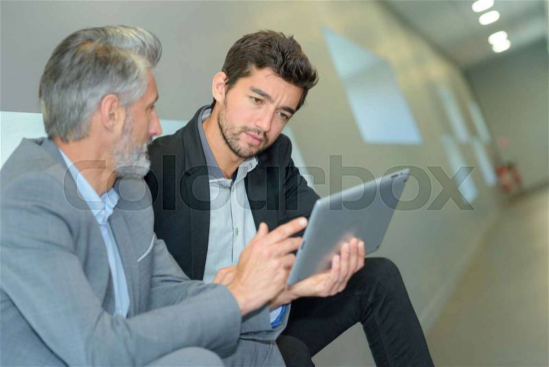 Company workers looking a tablet at a corridor, stock photo