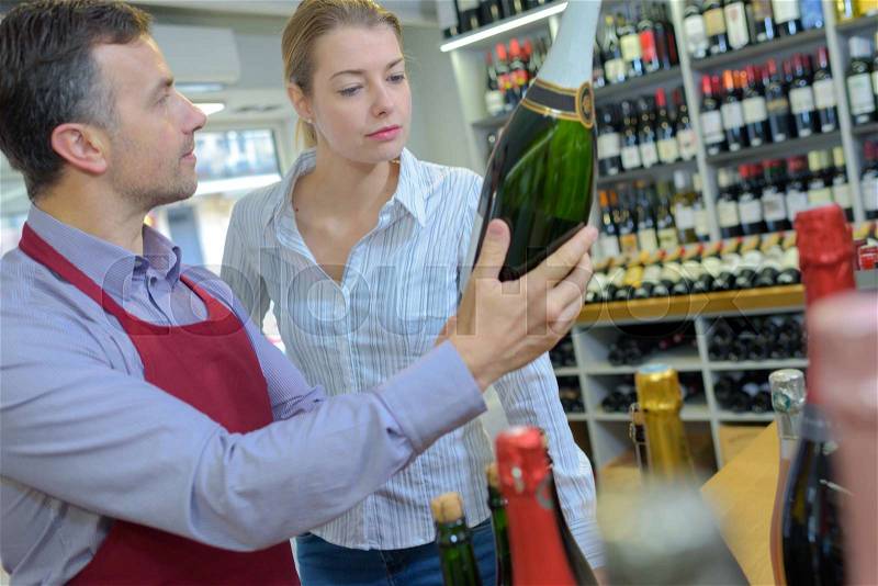 Sommelier in wine store giving woman recommendation for champagne, stock photo