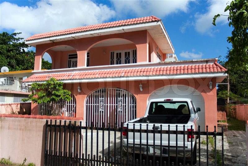 A pink Caribbean style home with a garage and gated driveway, stock photo