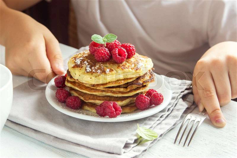 Child eating healthy breakfast at home - pancakes with raspberries on plate with children hands, stock photo