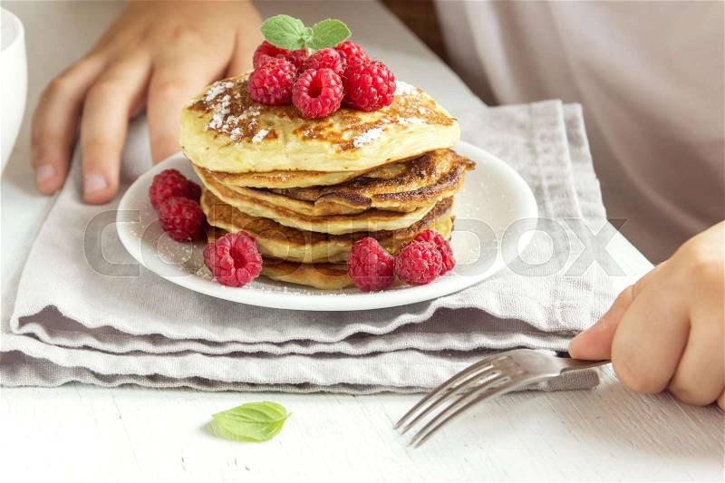 Child eating healthy breakfast at home - pancakes with raspberries on plate with children hands, stock photo
