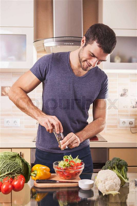 Young man preparing food at home in kitchen using pepper-mill, stock photo