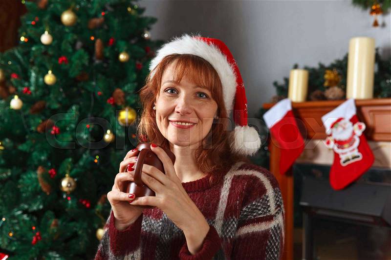 Woman with mug in the room with fireplace and Christmas decorations, stock photo