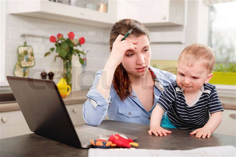 Young mother working with her baby at home, stock photo