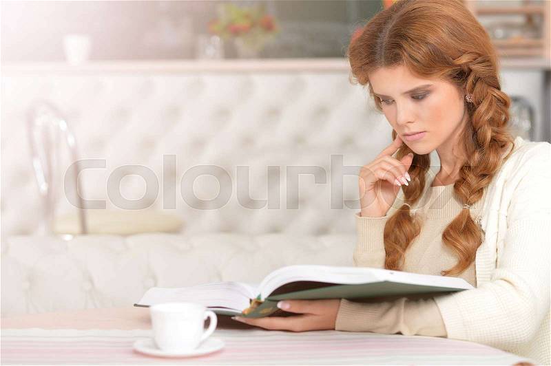 Portrait of beautiful red haired woman reading a book at home, stock photo