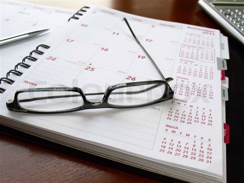 Monthly planner with reading glasses and pen on the table, stock photo