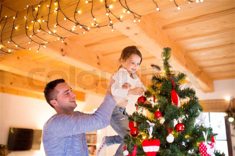 Young father holding his little daughter in his arms at home decorating Christmas tree together, stock photo