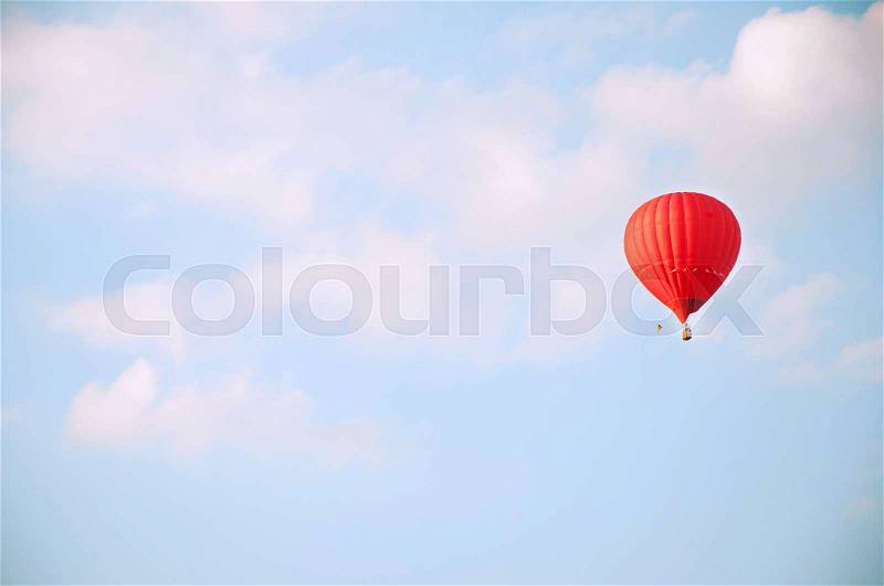 Red hot air balloon flying in blue sky with white clouds, stock photo