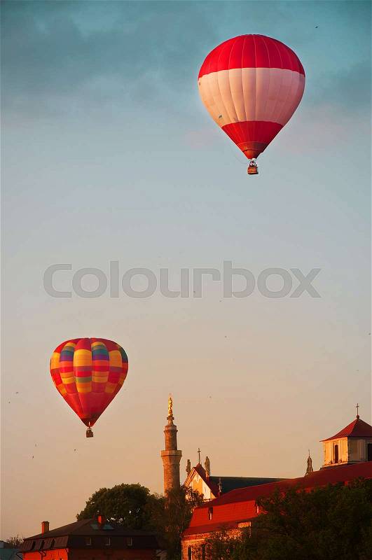 Red hot air balloons flying in blue sky with white clouds over Kamianets-Podilskyi city, stock photo
