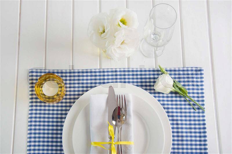 Table setting with blue checkered tablecloth, white napkin, silverware, yellow decoration and flowers, stock photo