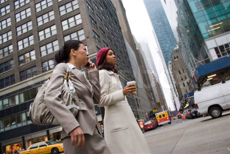 Two business women walking in the big city One woman is on her cell phoneSlightly shallow depth of field, stock photo