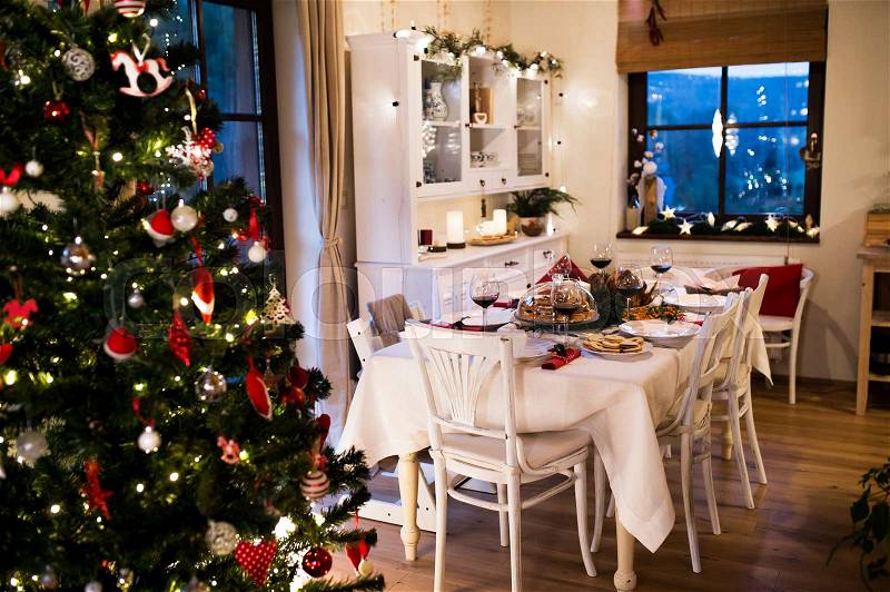 Christmas meal laid on table in decorated dining room. Roasted turkey or chicken, cookies, Christmas tree, plates and glasses of red wine, stock photo