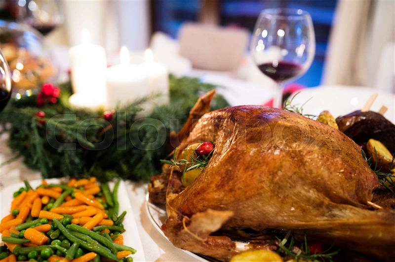 Christmas meal laid on table in decorated dining room. Roasted turkey or chicken, vegetables, Christmas wreath, glass of red wine, stock photo