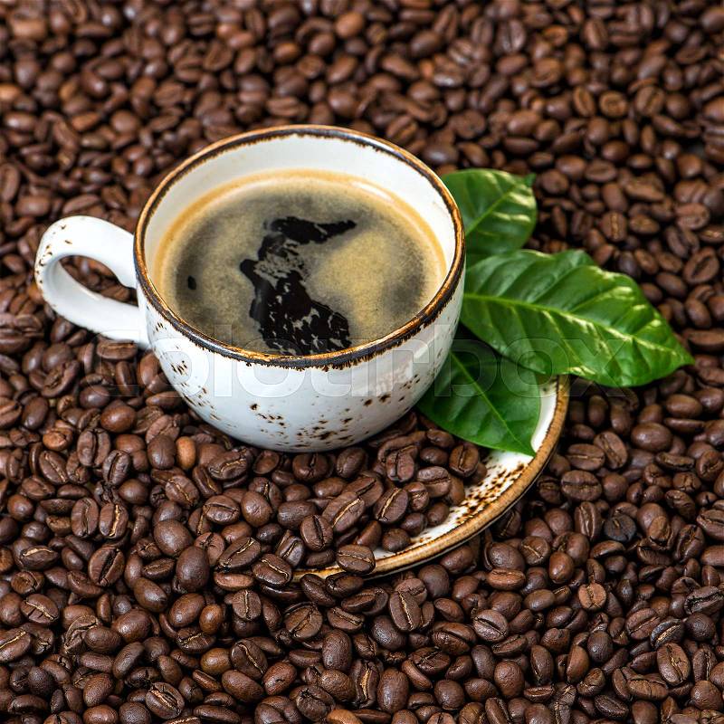 Black coffee with green leaves on coffee beans background square, stock photo