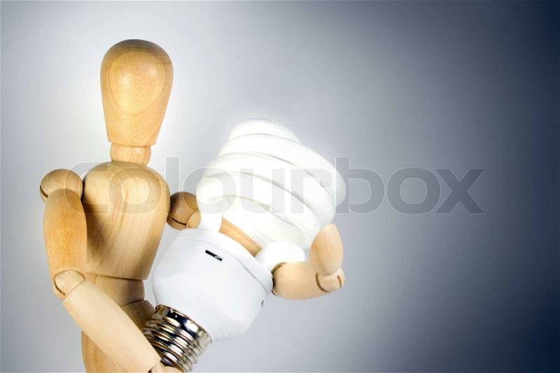 A wooden model grasping a compact fluorescent light bulb. Great for energy savings or going green concepts, stock photo