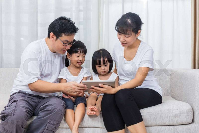 Asian Chinese parents and daughters using tablet on the sofa in the living room at home, stock photo