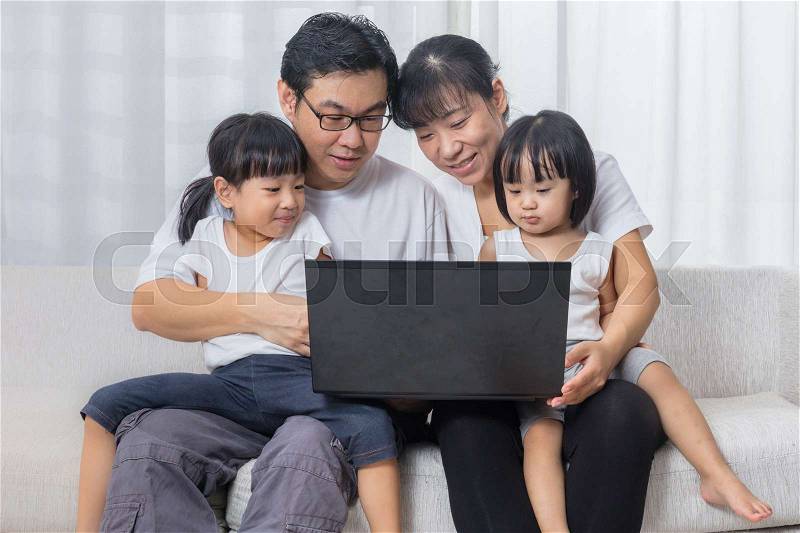 Asian Chinese parents and daughters using laptop on the sofa in the living room at home, stock photo