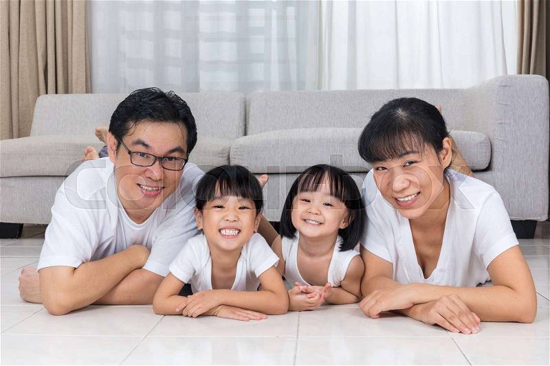 Happy Asian Chinese parents and daughters lying on the floor in the living room at home, stock photo