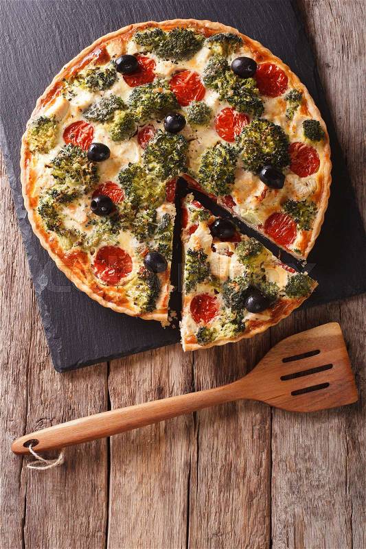 Savory Pie: Sliced Quiche with chicken, broccoli, tomatoes and olives close-up on the table. Vertical view from above\, stock photo