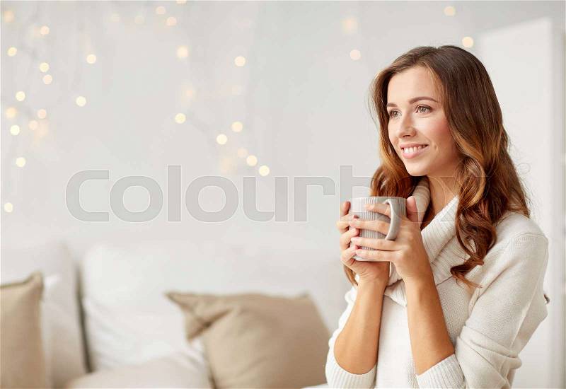 Morning, leisure, christmas, winter and people concept - happy young woman with cup of coffee or tea at home, stock photo