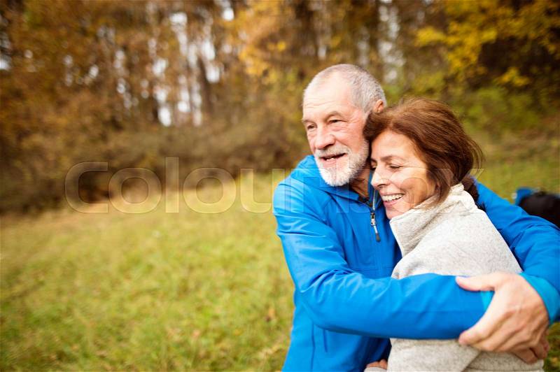 Beautiful active senior runners hugging outside in sunny autumn forest, stock photo