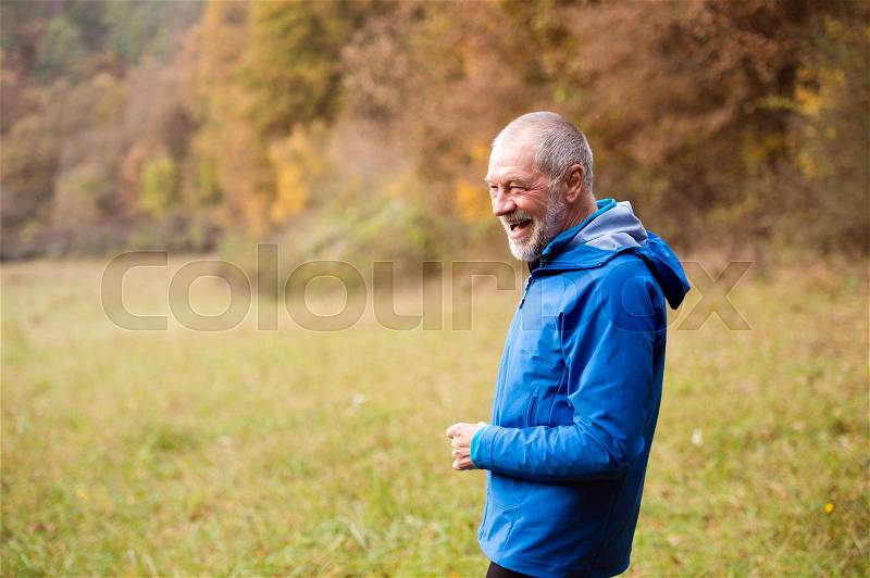 Senior runner in blue jacket resting outside in sunny autumn nature, laughing, stock photo