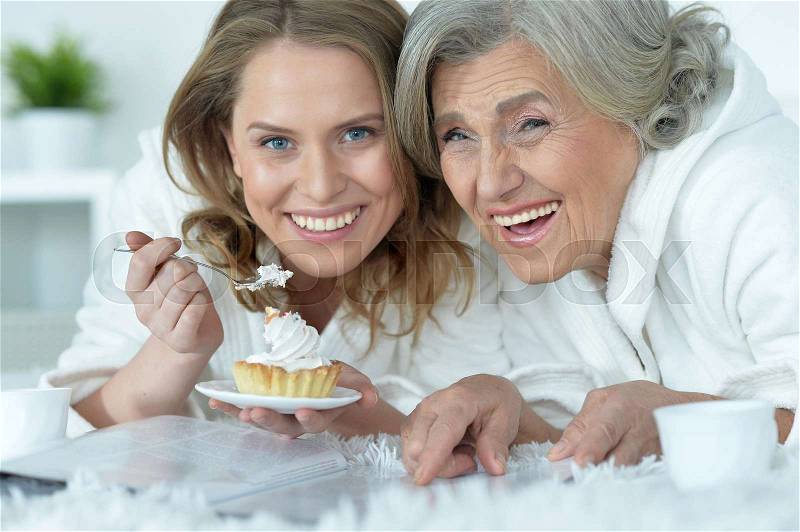 Portrait of senior woman with her adult daughter eat tasty cake and reading magazine, stock photo