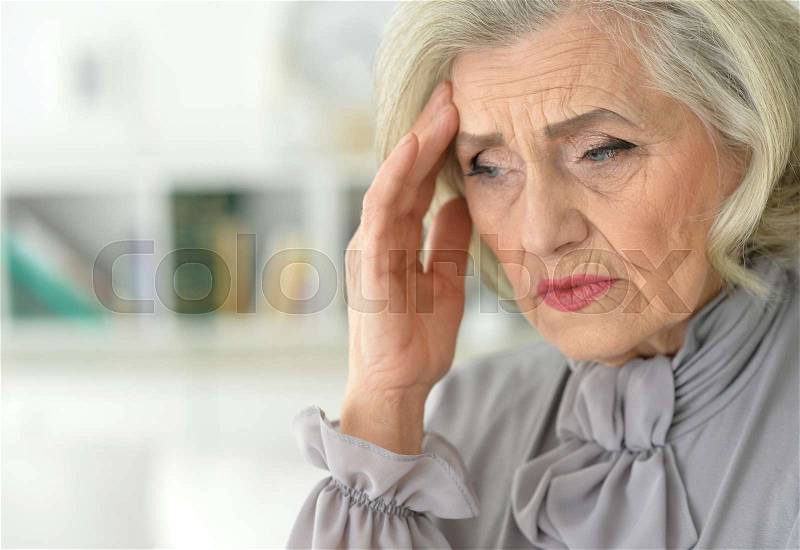 Portrait of senior woman in grey blouse with headache, stock photo