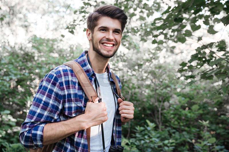 Side view of smiling man with backpack in forest. holds on to the harness. man in shirt, stock photo