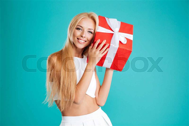 Portrait of a happy wondered woman holding gift box isolated on the blue background, stock photo