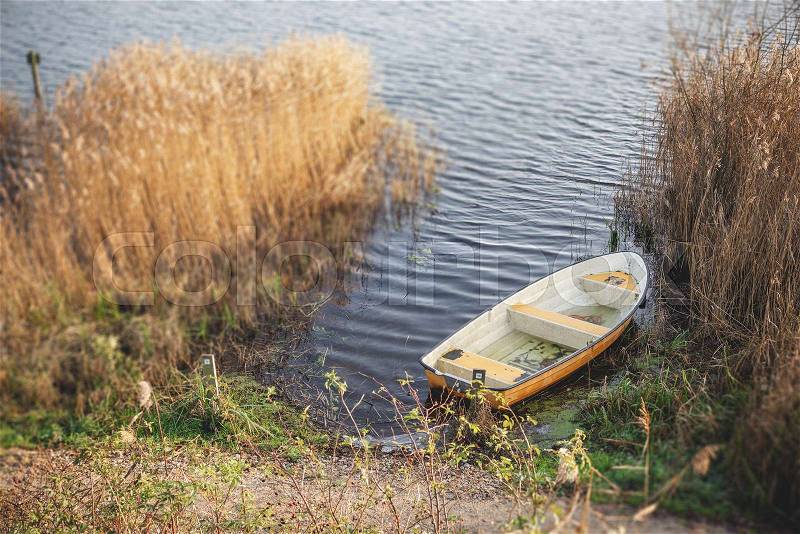 Yellow fishing boat in a dark lake in the autumn season surrounded by colorful reeds in the water, stock photo
