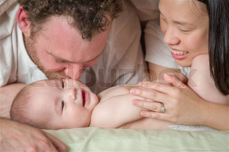 Mixed Race Chinese and Caucasian Baby Boy Laying In Bed with His Father and Mother, stock photo