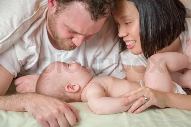 Mixed Race Chinese and Caucasian Baby Boy Laying In Bed with His Father and Mother, stock photo