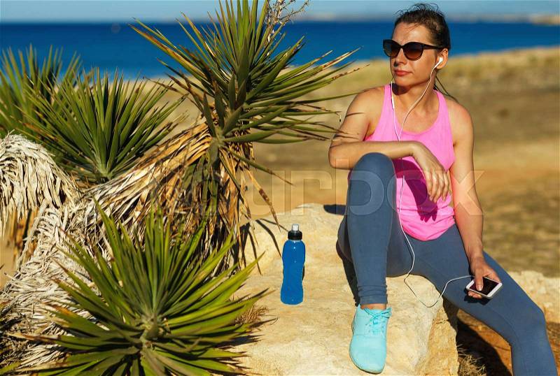 Sport girl resting after jogging on the rock by the sea, stock photo