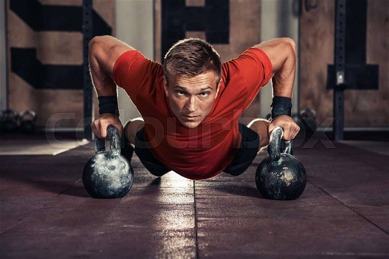 Handsome muscular man doing push ups on kettle ball in gym, stock photo