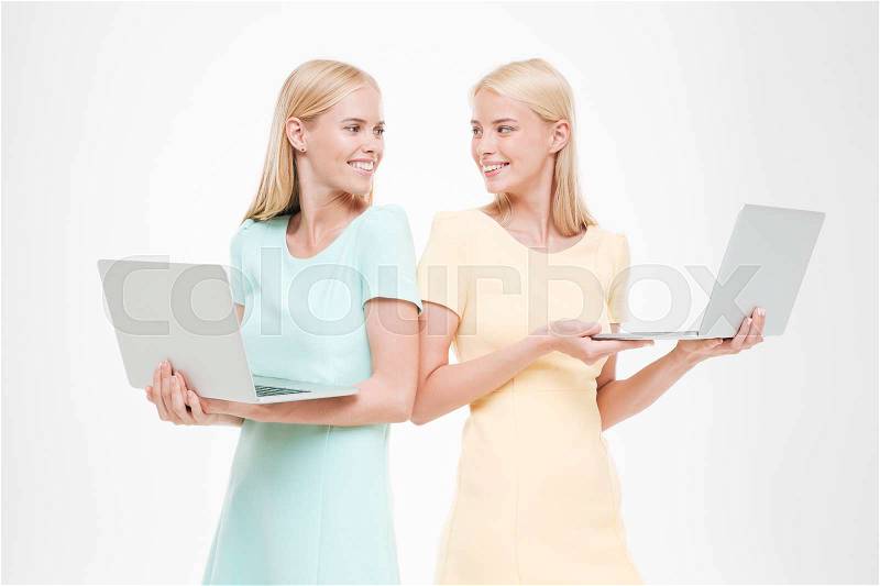 Picture of two young women looking at each other and holding laptops. Isolated over white background, stock photo