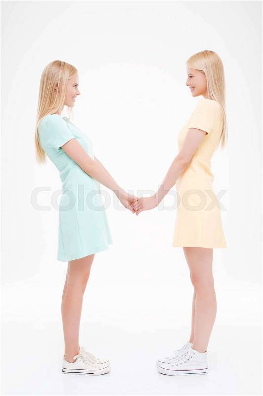 Photo of two girls holding each other by hands. Isolated over white background, stock photo