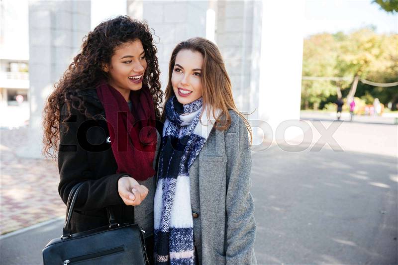 Portrait of two beautiful young women wearing scarfs communication. Holding bags. Against nature background. Look aside, stock photo