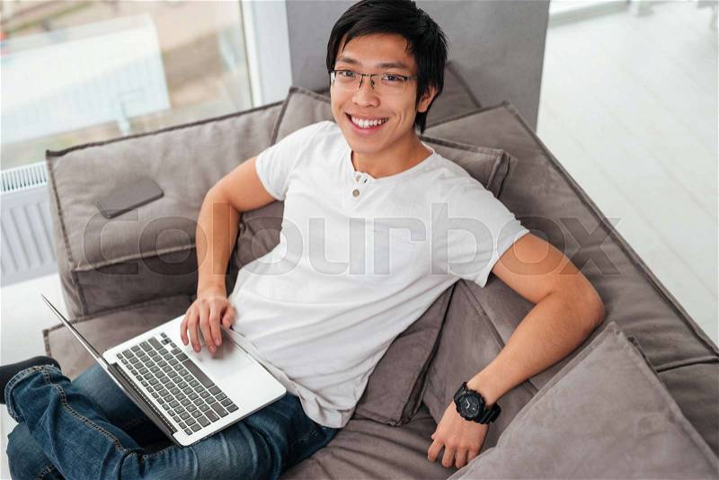 Above portrait of asian man with laptop on sofa. looking at camera, stock photo