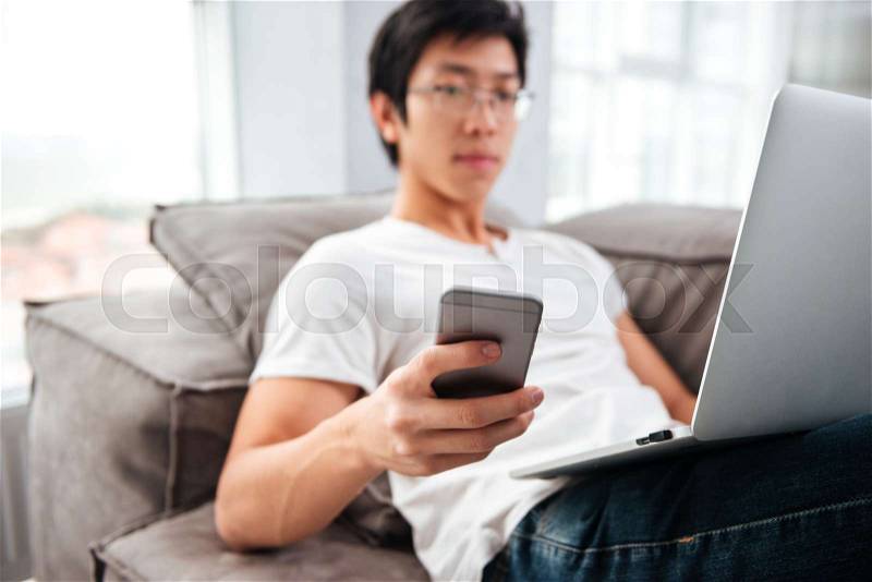 Asian man with laptop and phone on sofa. side view, stock photo
